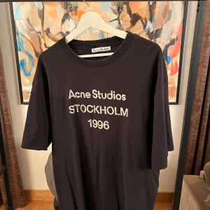 Svart Acne Studios t-shirt Stockholm - Svart t-shirt från Acne Studios med tryck 'Acne Studios STOCKHOLM 1996' på bröstet. Oversized passform, storlek L.
