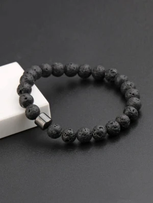 Svart Armband - Bilderna visar ett svart armband med runda lavastenpärlor och en metallisk detalj.