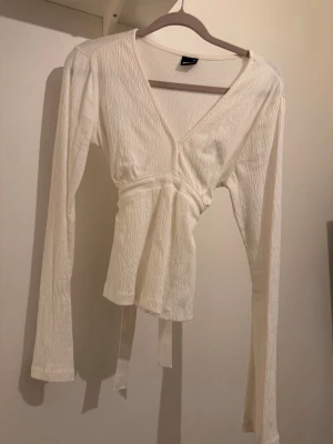 Vit omlottopp med v-ringning - Vit omlottsttopp från Ginatricot. Finns band så man kan knyta där bak. Använd ca 5 gånger totalt. 