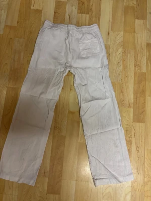 Vita linnebyxor med resårmidja - Säljer ett par vita linnebyxor med avslappnad passform och resår i midjan. Byxorna har fickor fram och en bakficka, raka ben och är gjorda i ett lätt och luftigt linnematerial. Perfekta för chill dagar när du vill ha något bekvämt och stilrent.
