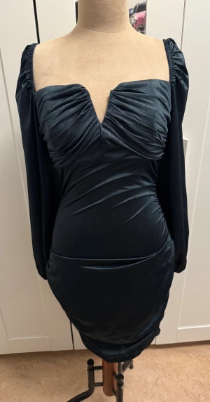 Marinblå omlottklänning från Bubbleroom - Snygg marinblå kortklänning från Bubbleroom i mjuk och glansig polyester. Klänningen har långärmade puffärmar, omlottdetalj vid bysten och v-ringad hals. Figurnära passform som framhäver siluetten och ger en trendig look.