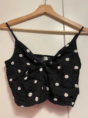 croppat polkadot linne - kort, svart linne med vita prickar! toppen har en knytdetalj vid bysten, justerbara axelband och är ribbad vid ryggen.