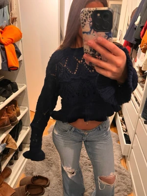 Mörkblå croppad stickad tröja - Säljer en mörkblå croppad stickad tröja med snyggt hålmönster och breda, långa ärmar. Tröjan har ribbade muddar och en cool, lite oversized passform 