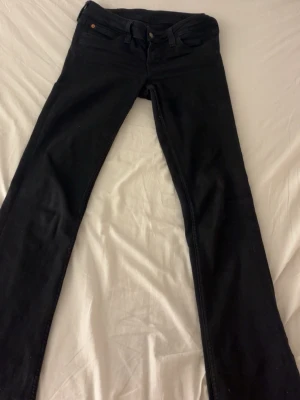 Svarta lågmidjade jeans från Cheap Monday - Säljer ett par svarta jeans från Cheap Monday med klassisk femficksdesign och en lila etikett med logga bak på midjan. Jeansen har bootcut passform och mycket låg midja, tillverkade i jeansmaterial. Säljer dessa eftersom de är lite för stora för mig i midjan, storlek 28 längd 34. Är perfekta för dig som älskar lågmidjade snygga jeans! 