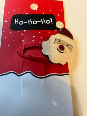 Julig hårklämma med tomte - Säljer en söt hårklämma med en glittrig tomtefigur framtill. Klämman har röd tygdetalj och tomten har vitt ansikte, röd näsa och röd mössa. Perfekt accessoar för att piffa upp håret under julen!