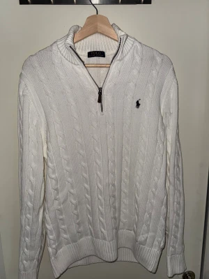 Vit stickad tröja Polo Ralph Lauren - Säljer en vit stickad tröja från Polo Ralph Lauren i storlek L. Tröjan har kabelstickat mönster, half zip-dragkedja och ribbad krage. Klassisk logga broderad på bröstet. Köpt 23november