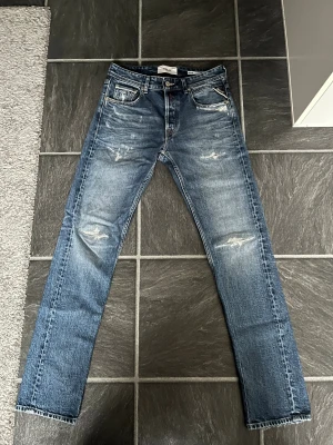 Replay Grover blå jeans med slitningar - Säljer ett par Replay Grover jeans i blå tvätt med coola slitningar och detaljer. Klassisk femficksmodell med raka ben och normal passform. Jeansen har snygga kontrastsömmar och Replay-logga på fickan. Perfekt för dig som gillar en avslappnad stil. Jag tycker att dem är 8/10 i skick jag har använt dem lite men är fortfarande i väldigt bra skick.