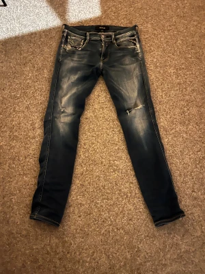 Replay Anbass skinny jeans blå - Säljer ett par Replay Anbass jeans i skinny fit med snyggt slitna detaljer och dragkedja. Färgen är mörkblå med ljusare tvätt och klassiska fem fickor. Märkespatch bak och Replay-logga vid fickan. Perfekt för dig som gillar smalare jeans med cool look. passar dig som är 180, 70kg