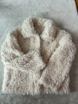 Krämvit teddyjacka från Kappahl - Säljer en fluffig och supermjuk teddyjacka från Kappahl i krämvit färg. Jackan har en klassisk krage och långa ärmar, perfekt för dig som vill ha en cozy look. Materialet är syntetiskt och ger en riktigt gosig känsla.