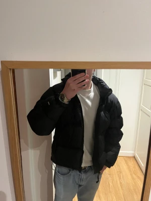 Svart pufferjacka från The North Face - Säljer en svart pufferjacka från The North Face med hög krage och dragkedja framtill. Jackan har en clean look med logga på bröstet och ryggen, samt breda quiltade sektioner. Perfekt för kalla dagar och riktigt snygg till jeans.
