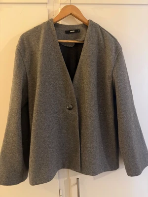 Grå kappa från Bikbok  - Säljer en stilren grå kappa från Bikbok i storlek S. Jackan har en enkel knäppning med en knapp framtill, rak passform och långärmade ärmar. Materialet är mjukt och känns lyxigt, perfekt för dig som gillar minimalistisk vibe och vill hålla dig varm.