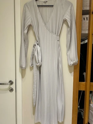  Ny Ljus omlottklänning från Bubbleroom - Säljer en ljus omlottklänning från Bubbleroom i storlek XS. Klänningen har plisserat tyg, v-ringad hals och långa ärmar med resår vid ärmslut. Materialet känns mjukt och har ett elegant fall. Perfekt för dig som gillar stilrena detaljer och modern look.