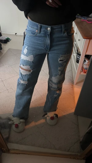 Low waist loose jeans från Nelly - Säljer ett par ljusblå jeans från Nelly i modellen low waist loose jeans. De har flera slitningar och hål framtill för en riktigt edgy vibe. Passformen är loose och benen är raka. Klassisk femficksdesign och knappgylf. 