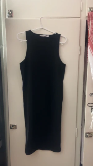 Svart ribbad långklänning 157 M - Svart ärmlös långklänning från 157 i storlek M. Klänningen har en ribbad struktur och en enkel, rak passform med hög hals. Perfekt för dig som gillar stilrena och minimalistiska plagg.