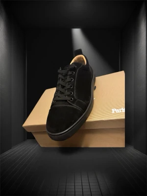 Svarta sneakers från Christian Louboutin - Säljer ett par svarta sneakers från Christian Louboutin med klassisk röd sula. Skorna har snörning, rund tå och är tillverkade i mjuk mocka med detaljer i skinn. Kommer med originalkartong och tillbehör. Perfekt för dig som gillar lyxiga och stilrena sneakers.