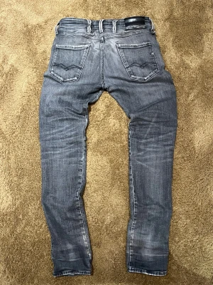 Replay Anbass grå jeans slim fit - Säljer ett par Replay Anbass jeans i grå tvätt med snygga slitningar. Slim fit-modell med låg midja och raka ben. Jeansen är använda några gånar ok är i bra sick! Skriv om ni har några fråger så är jag glad art få svara på dem🙌