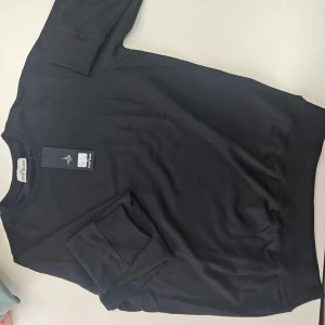 Svart sweatshirt från Stone Island HELT NY OCH ÄKTA MED KVITTO - Svart sweatshirt från Stone Island med klassisk rund hals och lång ärm. Ikonisk logopatch på vänster ärm ger en clean och stilren look. Perfekt för dig som gillar streetwear och vill ha något enkelt men ändå snyggt. Dm vid intresse