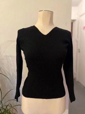 Svart ribbad stickad tröja v-ringad - Snygg svart stickad tröja med ribbad struktur och v-ringad hals. Tröjan har långärmade och en slim passform som sitter snyggt på kroppen. Perfekt för dig som gillar stilrena och enkla plagg med lite edge.