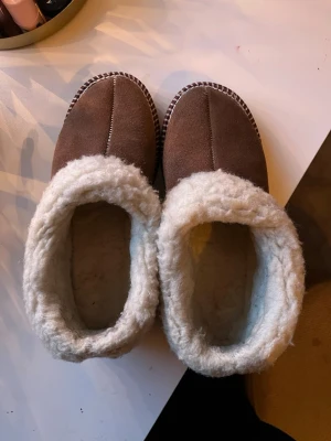 Bruna tofflor med vit fluffig kant - Säljer tofflor som jag köpt från Moheda toffeln för några år sedan, tofflorna är använda men o bra skick. Säljer pga att dem är små. Det har tillkommit lite ludd på vissa ställen på tofflorna.  Storleken är 37 om jag inte missminner mig och på hemsidan står det att dem kan vara små i storlek eftersom de är handgjorda. Har en mall på storlekarna från hemsidan så vid intresse kan jag skicka den. Tofflorna är i ull och textil mix på insidan + detaljen utan på. På utsidan är tofflorna i mocka  Nypri