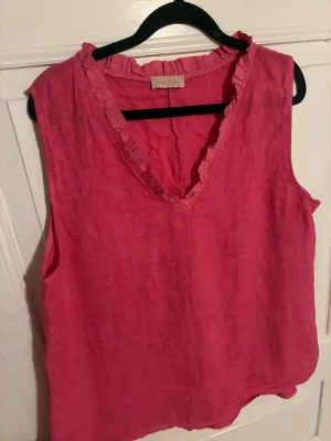 Rosa linnetopp från Chica London - Säljer en snygg rosa linnetopp från Chica London. Toppen är ärmlös med v-ringning och har volangdetaljer längs halsringningen. Perfekt för varma dagar och enkel att styla med jeans eller kjol.