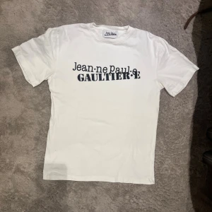 Vit Jean Paul Gaultier t-shirt - Säljer en vit t-shirt från Jean Paul Gaultier med svart tryck framtill. Denna t shirten är ovanlig och säljs inte längre av företaget.
