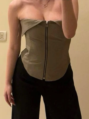 Khaki Corset top from Zara - Snygg khakigrön bandeau body med markerad krage upptill och dragkedja framtill. Kroppsnära passform och elastiska partier i sidorna för extra komfort. Perfekt för dig som vill ha en trendig och stilren look.