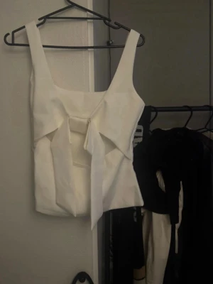 Vit linnetopp med knyt fram - Trendig vit linnetopp med breda axelband och snygg knytning framtill. Toppen har en rak, croppad passform och stilren design som passar till mycket. Perfekt för dig som vill ha en enkel men ändå unik topp till garderoben.