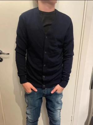 Mörkblå cardigan från These Glory Days - Snygg mörkblå cardigan från These Glory Days med knäppning framtill och långa ärmar. Klassisk och enkel design som passar till det mesta. Tillverkad i mjukt material för en bekväm känsla.