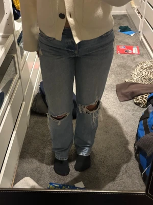 Blå raka jeans med slitningar - Säljer ett par ljusblå raka jeans med stora slitningar över knäna. Jeansen har klassisk femficksdesign och normal passform. Perfekta för en avslappnad och trendig look.