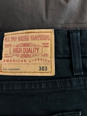 Svarta jeans från U.S. Top Denim - Svarta jeans från U.S. Top Denim Clothing med klassisk femficksdesign och raka ben. Jeansen har bälteshällor och en snygg läderpatch bak i midjan. Tillverkade i slitstarkt denim-material som passar perfekt till en avslappnad stil.