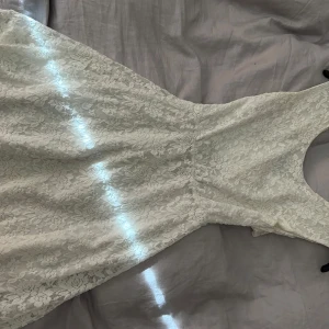 Studentklänning  - Säljer en elegant vit spetsklänning med ett vackert blommönster. Klänningen har en öppen rygg och är ärmlös, vilket ger en stilren look. Perfekt för student, konfirmation eller sommarens festligheter!💕