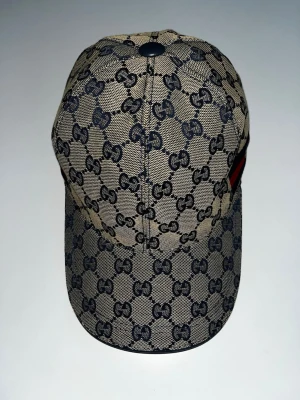 GG keps - Snygg beige keps med klassiskt GG-monogram i svart över hela kepsen. På sidan finns ett broderat band i rött och blått med ett litet tigerhuvud. Kepsen har böjd skärm och är tillverkad i ett slitstarkt tygmaterial. Skickar inom 24 timmar