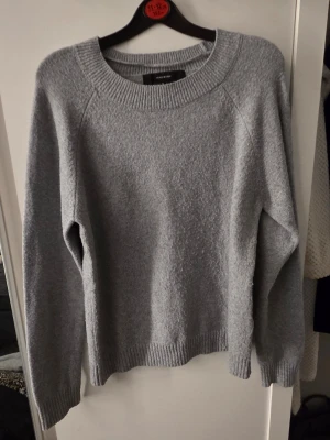 Grå stickad tröja från VERA MODA - Mysig grå stickad tröja från VERA MODA med rund halsringning och långa ärmar. Tröjan har ribbstickade muddar vid ärmslut och nederkant. Perfekt för lager-på-lager och enkel att matcha med olika outfits.