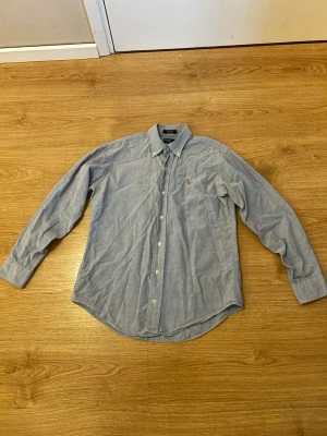 Ljusblå skjorta från Polo Ralph Lauren - NYRPIS Enligt ChatGPT: 1300kr-1600kr  Klassisk ljusblå skjorta från Polo Ralph Lauren i 100% bomull. Skjortan har button-down krage, långa ärmar och en liten broderad logga på bröstet. Perfekt till jeans eller chinos för en clean och stilren look.