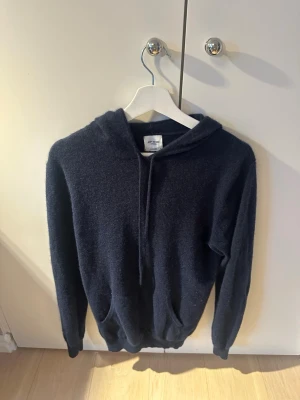 Mörkblå kashmir hoodie john henric - Mysig mörkblå hoodie med huva och snörning. Tillverkad i 100% kashmir som ger en skön och varm känsla. Klassisk passform med ribbade muddar vid ärmslut och nederkant. Perfekt för dig som gillar en enkel men stilren look.