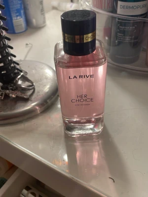 La Rive Her Choice parfym - La Rive Her Choice är en parfym för kvinnor med en elegant, rektangulär flaska i genomskinligt glas och ljusrosa. Endast testad