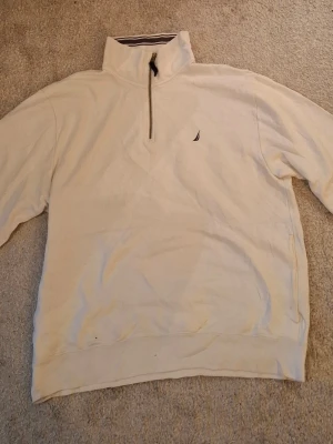 Nautica quarter-zip sweatshirt - En pullover med dragkedja/ quarter-zip sweatshirt från Nautica i vit bomull och polyester. Den har en kort dragkedja vid halsen och en broderad logga på bröstet.   Skick: Begagnad, mindre befläckning på ärmen (se bild 5). I övrigt bra skick