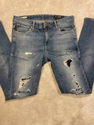 Jack n Jones jeans  - Feta Jack n Jones jeans med slitningar. Storleken står inte direkt men de sitter som 29/32, 30/32. De är bara skriva man vill ha måtten på dom! Jeansen är i bra skick förutom hål i vänster ficka, därav de låga priset! 