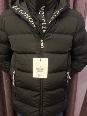 Svart dunjacka från Moncler - Svart dunjacka från Moncler med hög krage och dragkedja framtill. Jackan har två sidofickor med dragkedja och tydlig Moncler-logga på insidan av kragen. Perfekt för kalla dagar.