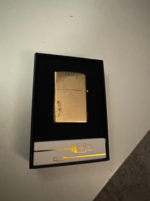 Guldfärgad USB-tändare i presentask - Säljer en guldfärgad USB-tändare i metall med solmönster på framsidan. Tändaren kommer i en svart presentask tillsammans med en laddningskabel. Perfekt för dig som vill ha en stilren och laddningsbar tändare.                                                           Pris kan diskuteras 