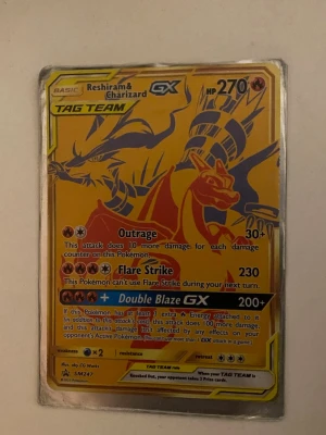 Pokémonkort Reshiram & Charizard GX - Säljer ett samlarkort från Pokémon med Reshiram & Charizard GX. Kortet har en guldfärgad bakgrund och visar båda Pokémon i en dynamisk pose. Det är en TAG TEAM GX-kort med flera attacker och HP 270. Perfekt för samlare eller Pokémon-fans.