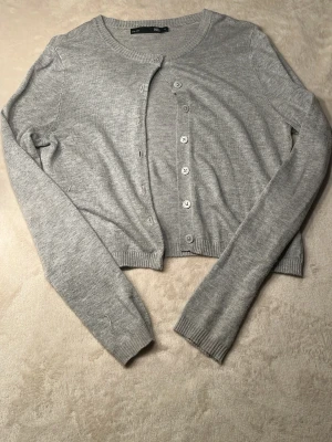 Grå cropped kofta med knappar - Stilren grå kofta från Lager 157 i mjukt stickat material. Croppad modell med rund halsringning och knäppning framtill. Perfekt att styla över en topp eller klänning för en trendig look.