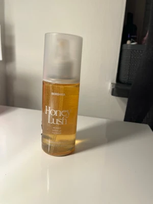 Bershka Honey Lush parfymmist - Fräsch parfymmist från Bershka i doften Honey Lush med inslag av honung, vanilj och blomnoter. Flaskan är genomskinlig med guldfärgad vätska och har en frostad vit spraykork. Perfekt för dig som gillar söta och blommiga dofter.
