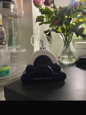 Ariana Grande Cloud parfym - Säljer en Ariana Grande Cloud parfym med en unik flaska i form av ett vitt och blått moln. Flaskan har en rund, vit kropp och står i ett mörkblått molnformat ställ. Snygg och modern design som sticker ut på parfymhyllan.