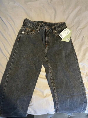 Grå jeans straight fit low waist - Snygga grå jeans straight fit low waist med klassisk straight fit och femficksdesign. Jeansen har orangea sömmar och silverfärgade nitar. Tillverkade i slitstarkt bomullsjeansmaterial. Perfekta för en avslappnad och trendig look.