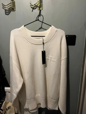 Vit stickad tröja från Axel Arigato - Kolla in denna krispigt vita stickade tröja från J.Lindeberg! Oversized fit med bred ribbad krage, muddar och nederkant. Diskret broderad logga på bröstet. Perfekt för lager-på-lager och chill vibes. Säljer då den är Köpt i fel storlek. 