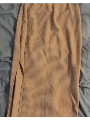 Beige ribbad kjol med slits - Trendig beige kjol i ribbat material med en snygg slits på sidan. Kjolen har en rak passform och är perfekt för dig som gillar stilrena plagg med en twist. Passar till både sneakers och boots.