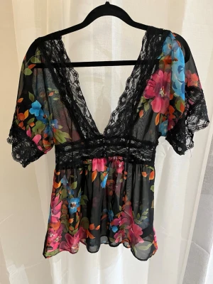 Blommig transparent blus med spets - Djup V-ringning med spetsdetaljer och korta ärmar med spetskant