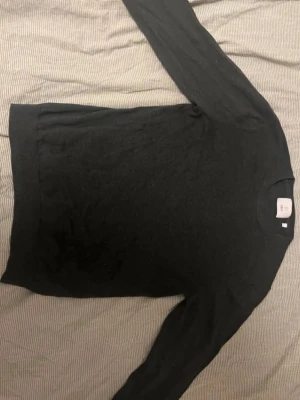 Mörk grön stickad tröja från Bläck - En stilren mörk grön stickad tröja från Bläck med rund halsringning och långa ärmar. Tröjan har ribbstickade muddar vid ärmslut och nederkant, perfekt för lager-på-lager och enkel att matcha med olika outfits.