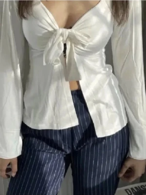 Vit omlottopp från Design by Si - Säljer en vit omlottopp från Design by Si i storlek XS/S. Toppen har lång ärm, djup v-ringning och knyt framtill. Tillverkad i mjuk bomull som känns skön mot huden. 